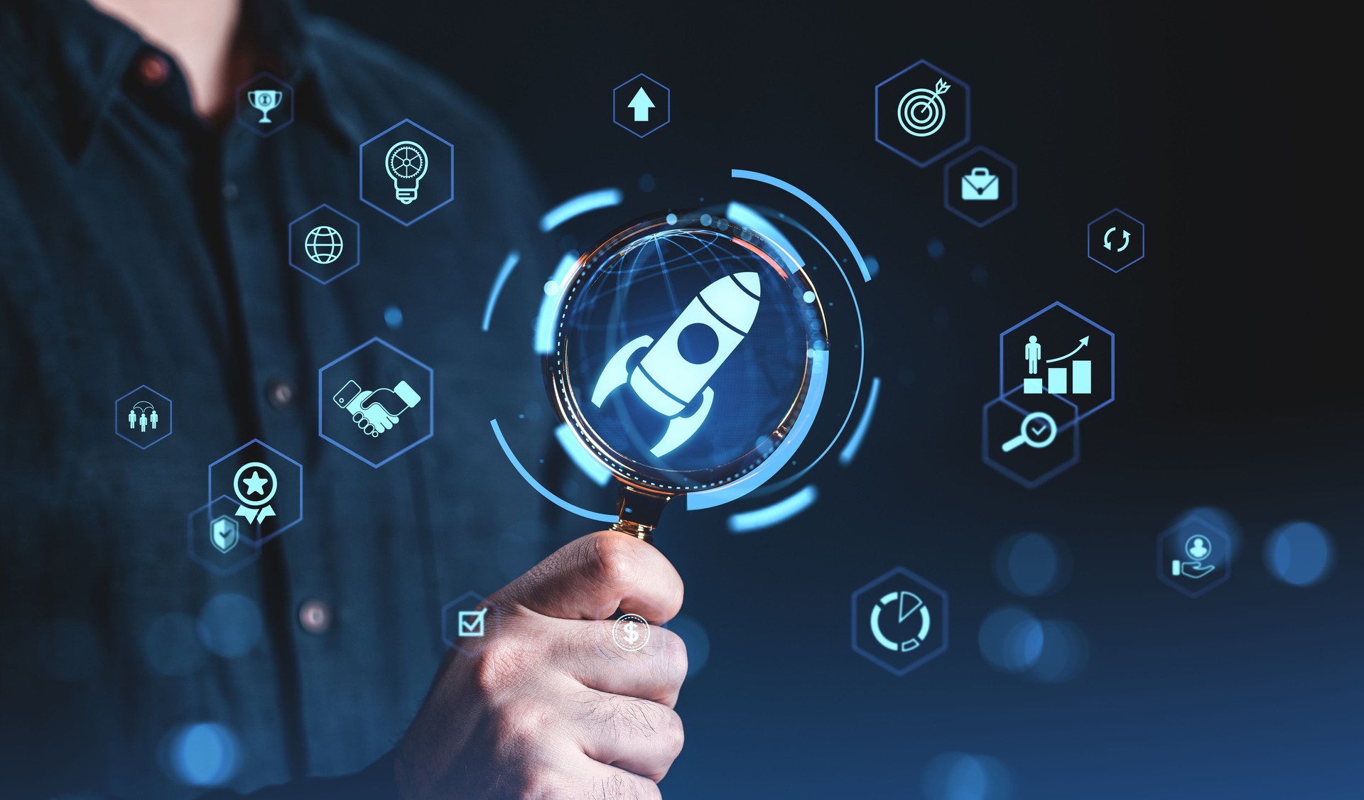 Businessman holding magnifying glass focused on rocket icon with futuristic startup and innovation concept icons in blue digital interface on dark background.